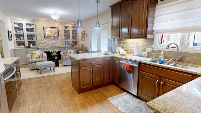 kitchen with light stone counters, a peninsula, a sink, light wood-style floors, and dishwasher