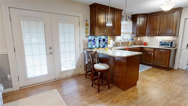 kitchen featuring a breakfast bar, french doors, light wood finished floors, tasteful backsplash, and a peninsula