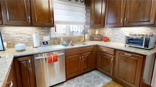 kitchen featuring light stone countertops, a toaster, a sink, stainless steel dishwasher, and decorative backsplash