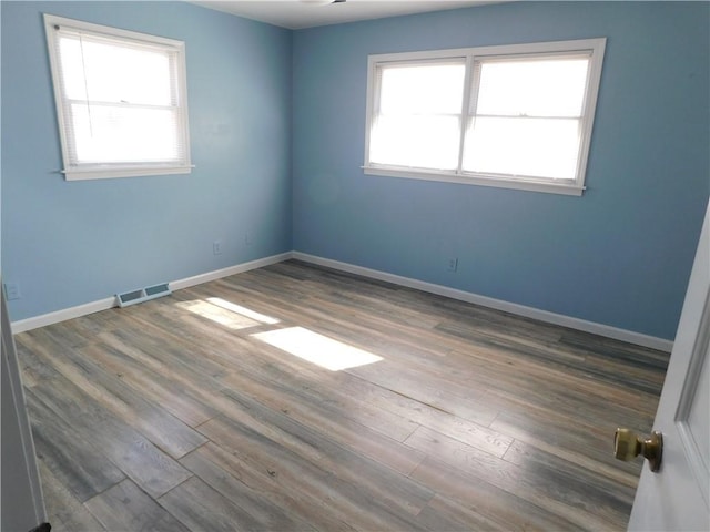 unfurnished room featuring visible vents, baseboards, and wood finished floors