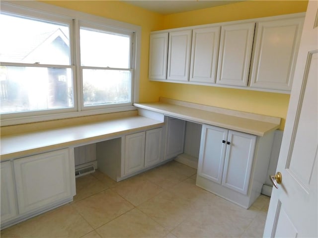 unfurnished office with light tile patterned floors, built in desk, and visible vents