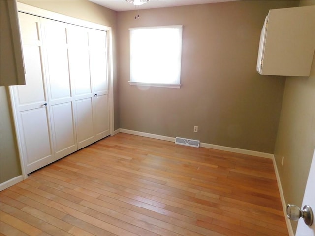 unfurnished bedroom with light wood finished floors, baseboards, visible vents, and a closet