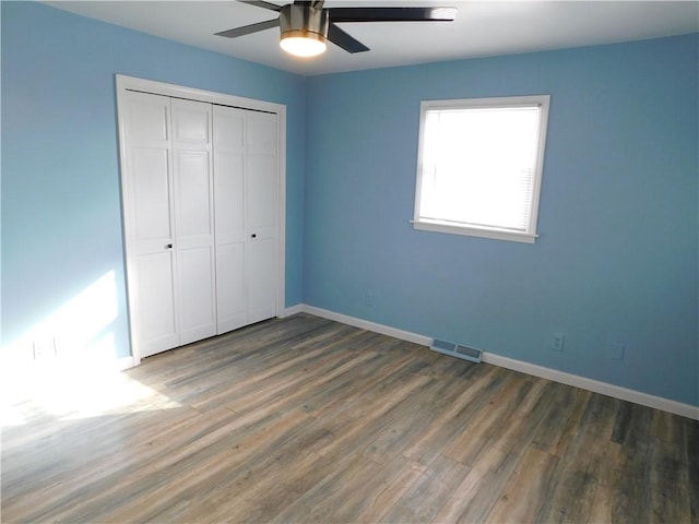 unfurnished bedroom with a closet, wood finished floors, visible vents, and baseboards