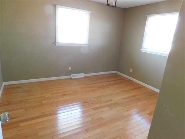 empty room with light wood-type flooring, visible vents, and baseboards