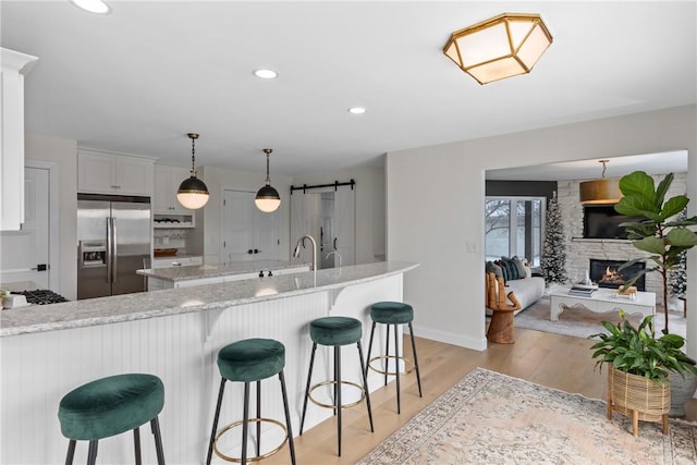 kitchen featuring pendant lighting, white cabinets, stainless steel built in refrigerator, light stone counters, and a breakfast bar