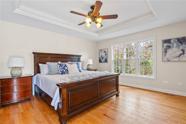 bedroom featuring light wood-style floors, a raised ceiling, crown molding, and visible vents