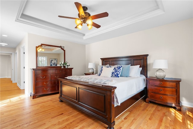 bedroom with light wood-style floors, ornamental molding, and a tray ceiling