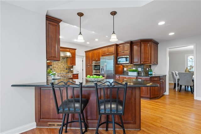 kitchen featuring wall chimney range hood, appliances with stainless steel finishes, decorative backsplash, and a peninsula