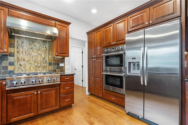 kitchen featuring decorative backsplash, wall chimney range hood, light wood-type flooring, recessed lighting, and appliances with stainless steel finishes