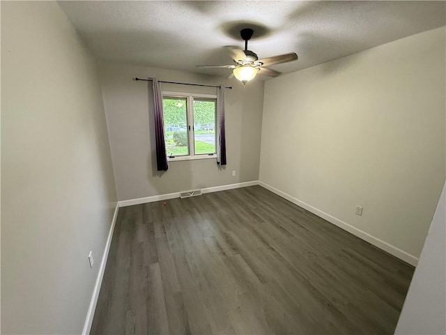 empty room featuring dark wood-style flooring, a ceiling fan, a textured ceiling, and visible vents