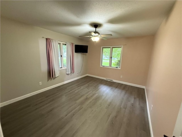 spare room featuring ceiling fan, visible vents, baseboards, and dark wood-type flooring