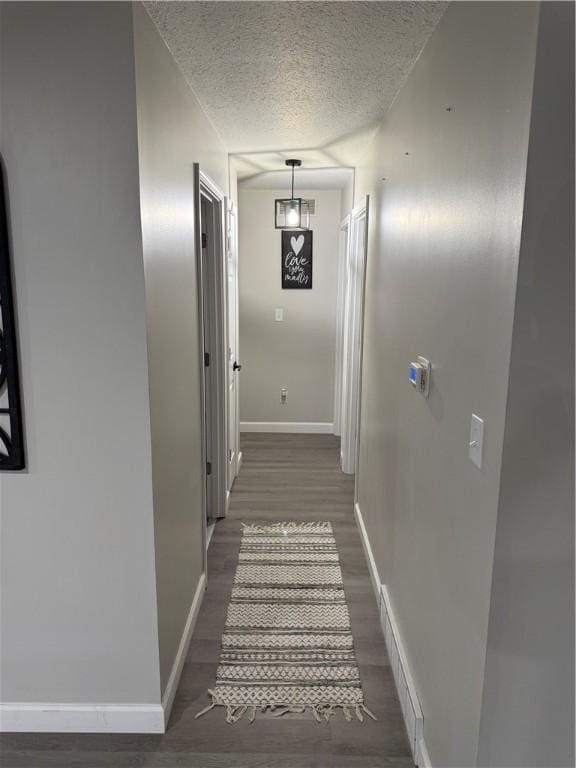 hallway with visible vents, a textured ceiling, baseboards, and wood finished floors