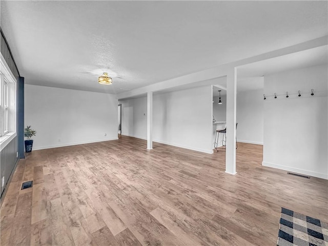 unfurnished living room featuring wood finished floors, visible vents, and baseboards