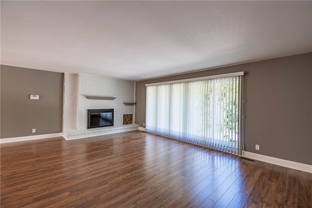 unfurnished living room with a brick fireplace and dark wood-type flooring