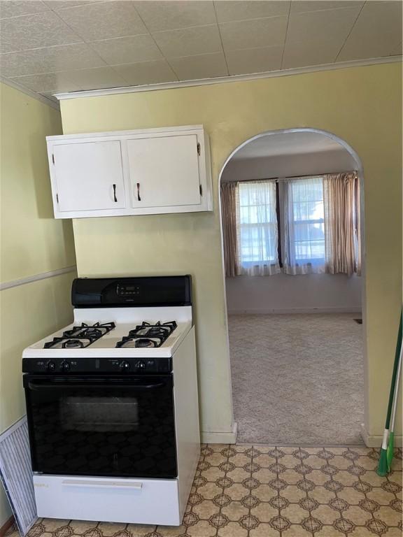 510 W Elm St, Hoopeston, IL 60942 - kitchen featuring white gas range oven, crown molding, white cabinetry, light carpet, and light floors