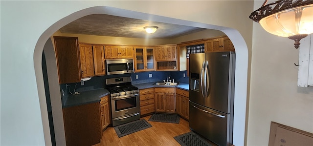 kitchen with decorative backsplash, stainless steel appliances, sink, decorative light fixtures, and light hardwood / wood-style flooring