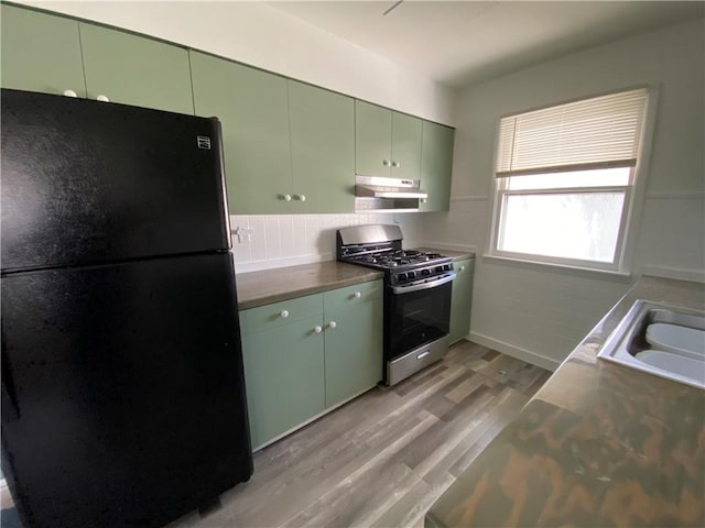 kitchen featuring stainless steel range with gas cooktop, light wood finished floors, green cabinets, freestanding refrigerator, and under cabinet range hood