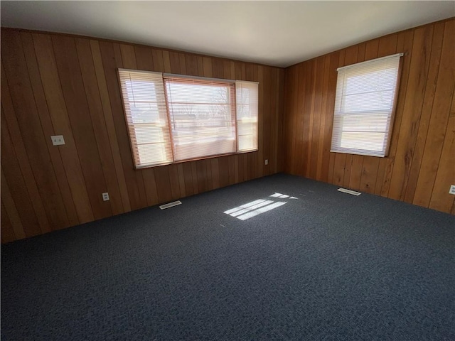 carpeted empty room featuring plenty of natural light, visible vents, and wooden walls