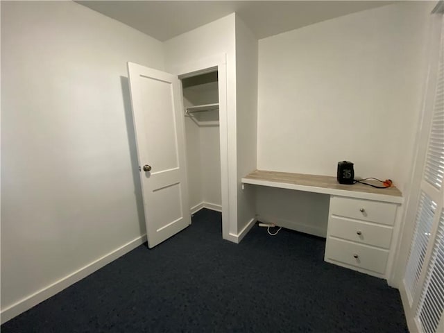 unfurnished office with dark colored carpet, built in desk, and baseboards