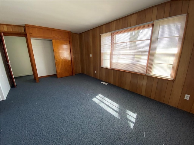 unfurnished bedroom featuring carpet floors, wood walls, visible vents, and a closet