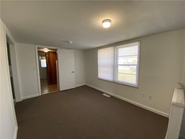 unfurnished room featuring visible vents, baseboards, and dark colored carpet