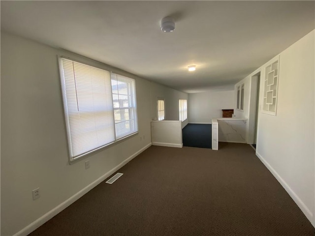 spare room with dark colored carpet, visible vents, and baseboards