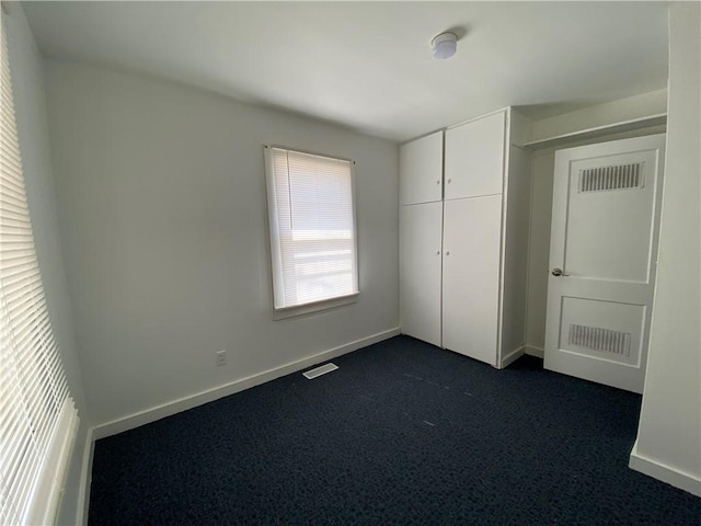 unfurnished bedroom with a closet, visible vents, dark carpet, and baseboards