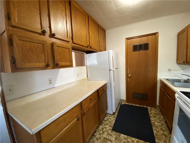 kitchen featuring light countertops, white appliances, brown cabinets, and a sink