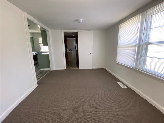 empty room with dark colored carpet, visible vents, and baseboards