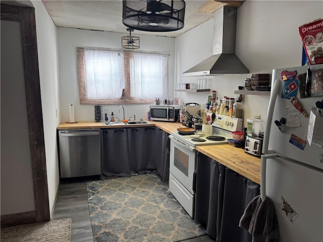 kitchen with wood counters, sink, stainless steel appliances, and wall chimney range hood