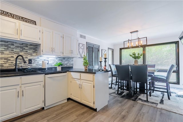 kitchen with light wood finished floors, dark countertops, white dishwasher, and a sink
