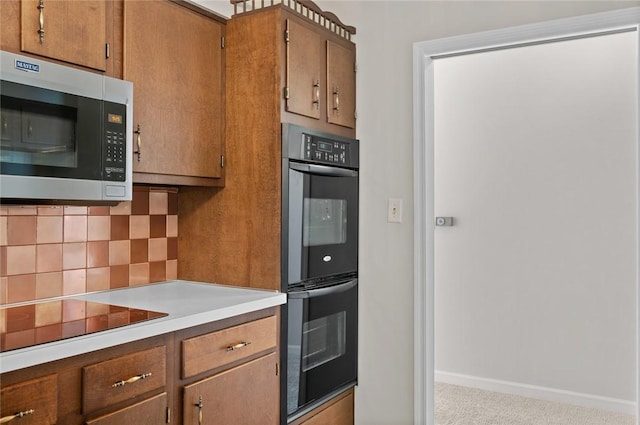 kitchen with stainless steel microwave, black electric stovetop, multiple ovens, tasteful backsplash, and light countertops