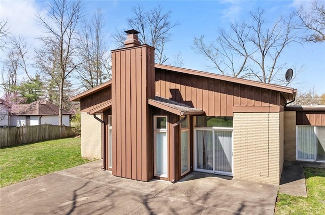 rear view of property featuring a chimney, a patio, brick siding, and board and batten siding
