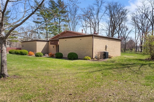 view of side of home featuring brick siding, a yard, cooling unit, and a chimney