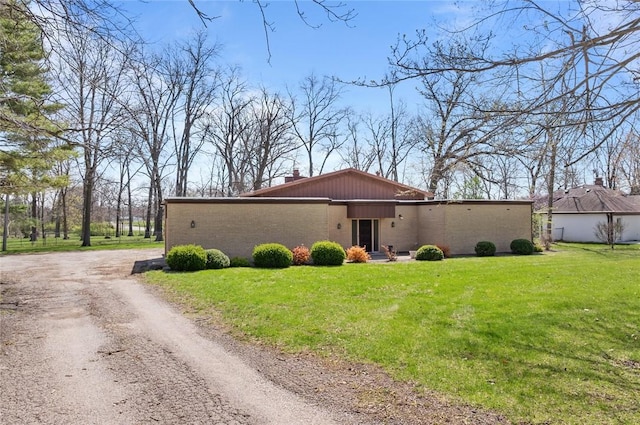 view of front facade with dirt driveway, a front yard, a chimney, and brick siding