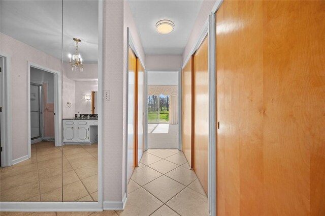 hall featuring a chandelier, light tile patterned flooring, and baseboards