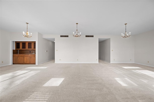 unfurnished living room with a chandelier, light carpet, and baseboards
