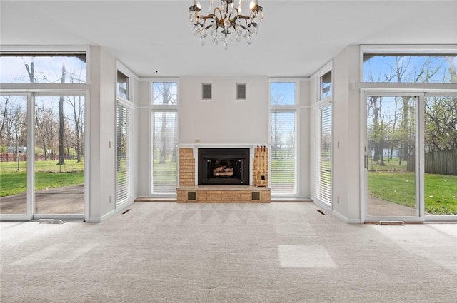 unfurnished living room with carpet, a chandelier, a brick fireplace, and baseboards