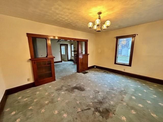 empty room featuring dark carpet, a healthy amount of sunlight, and a chandelier