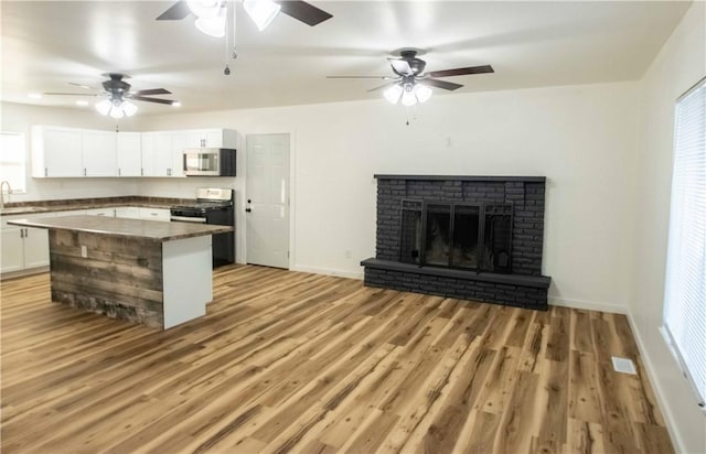 kitchen featuring stove, sink, light hardwood / wood-style flooring, a fireplace, and white cabinetry