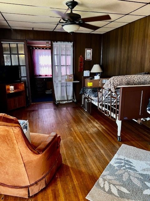 interior space with a paneled ceiling, wooden walls, ceiling fan, and dark wood-type flooring