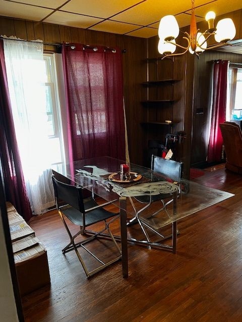 dining area with hardwood / wood-style flooring, a drop ceiling, wooden walls, and an inviting chandelier