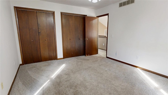 unfurnished bedroom featuring visible vents, carpet floors, two closets, and baseboards