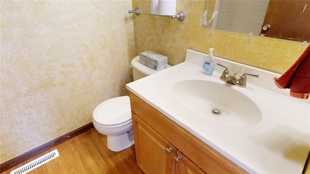 bathroom featuring visible vents, baseboards, toilet, wood finished floors, and vanity