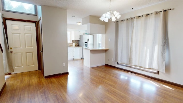 unfurnished dining area with visible vents, a textured ceiling, wood finished floors, an inviting chandelier, and baseboards