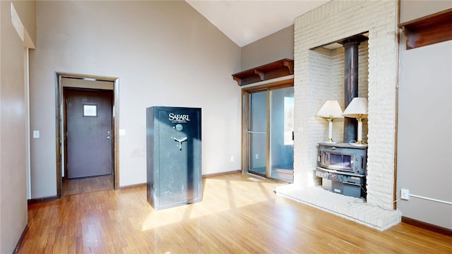 unfurnished living room featuring a wood stove, wood finished floors, baseboards, and high vaulted ceiling