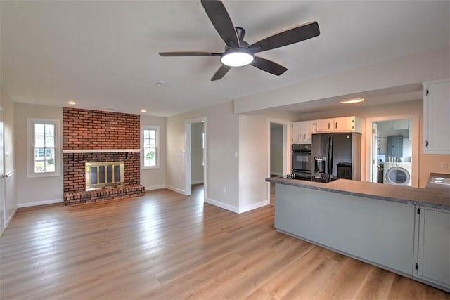 kitchen featuring a fireplace, washer / dryer, white cabinets, black appliances, and light wood-type flooring