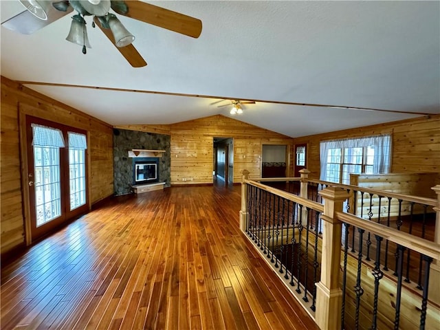 living room with hardwood / wood-style floors, wood walls, vaulted ceiling, and a stone fireplace