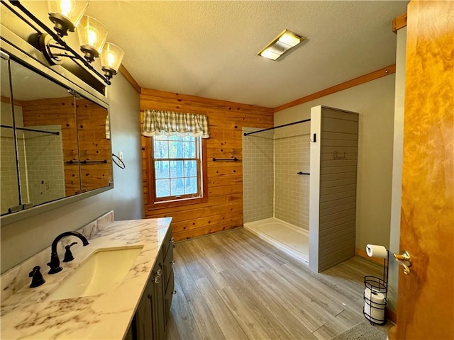 bathroom with wooden walls, a textured ceiling, tiled shower, wood-type flooring, and vanity