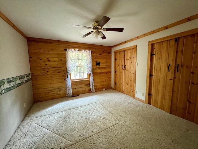 carpeted spare room featuring ornamental molding, wood walls, and ceiling fan